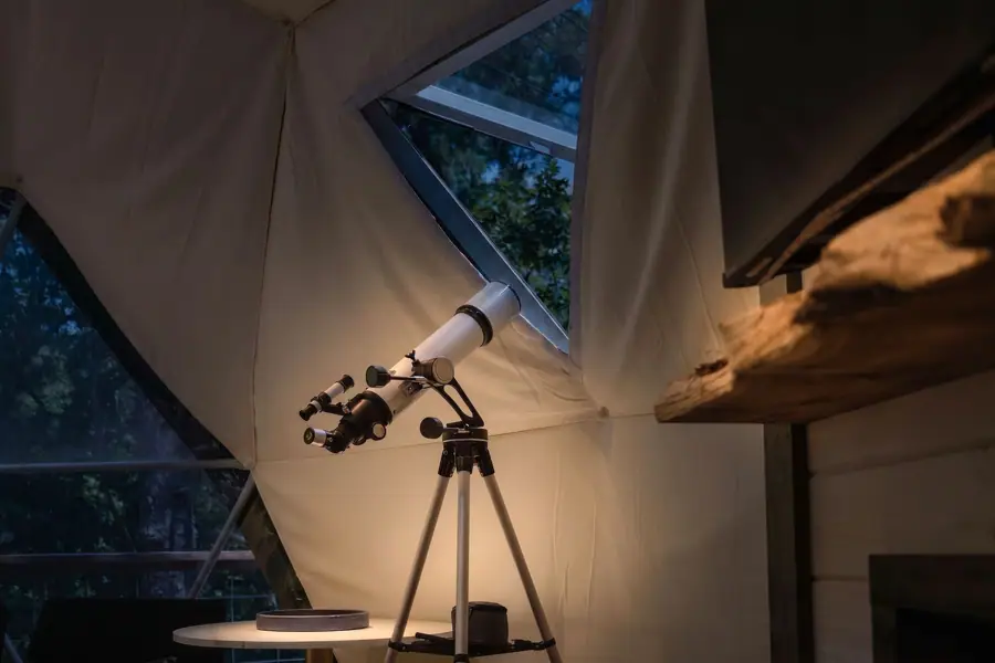 Telescope pointed through a triangular dome window at the trees