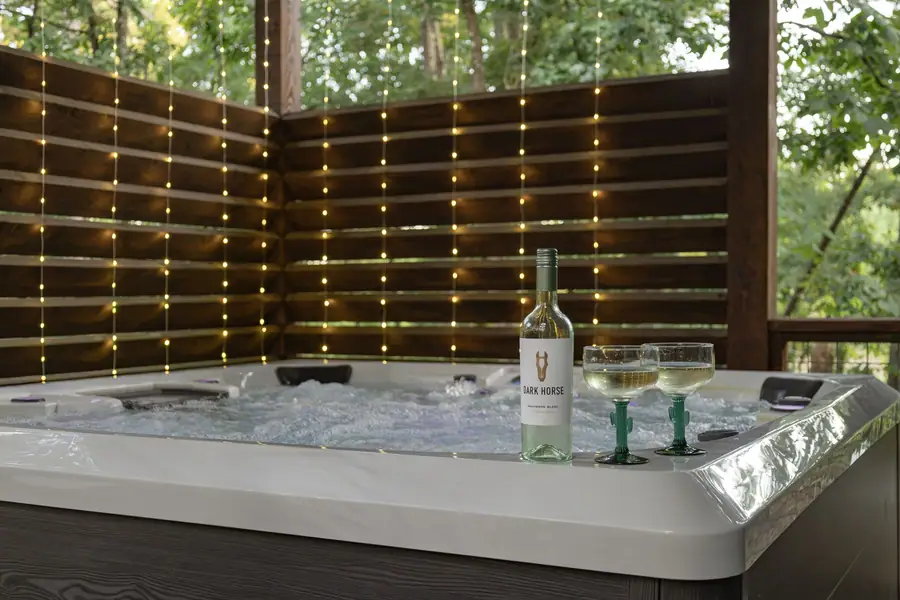 Bubbling hot tub with wine glasses under a lit privacy wall